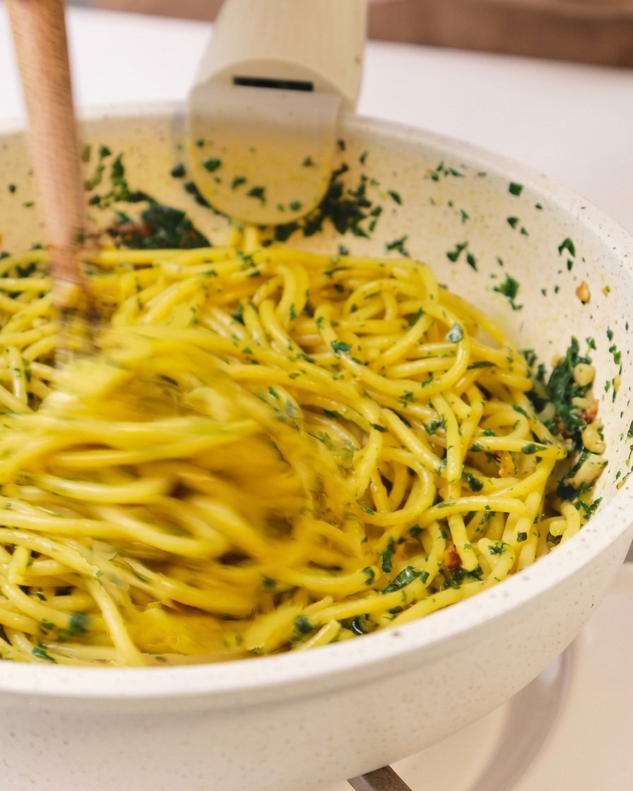 Dynamiczne ujęcie spaghetti mieszanego energicznie z ziołami i oliwą na patelni za pomocą drewnianych pałeczek.
