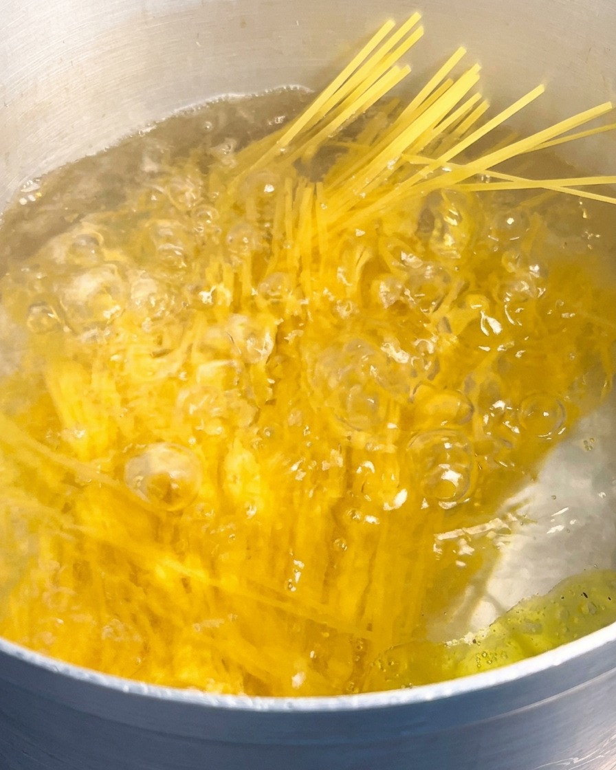 Porcja sucheho makaronu spaghetti zanurzana w dużym garnku z gwałtownie wrzącą wodą.