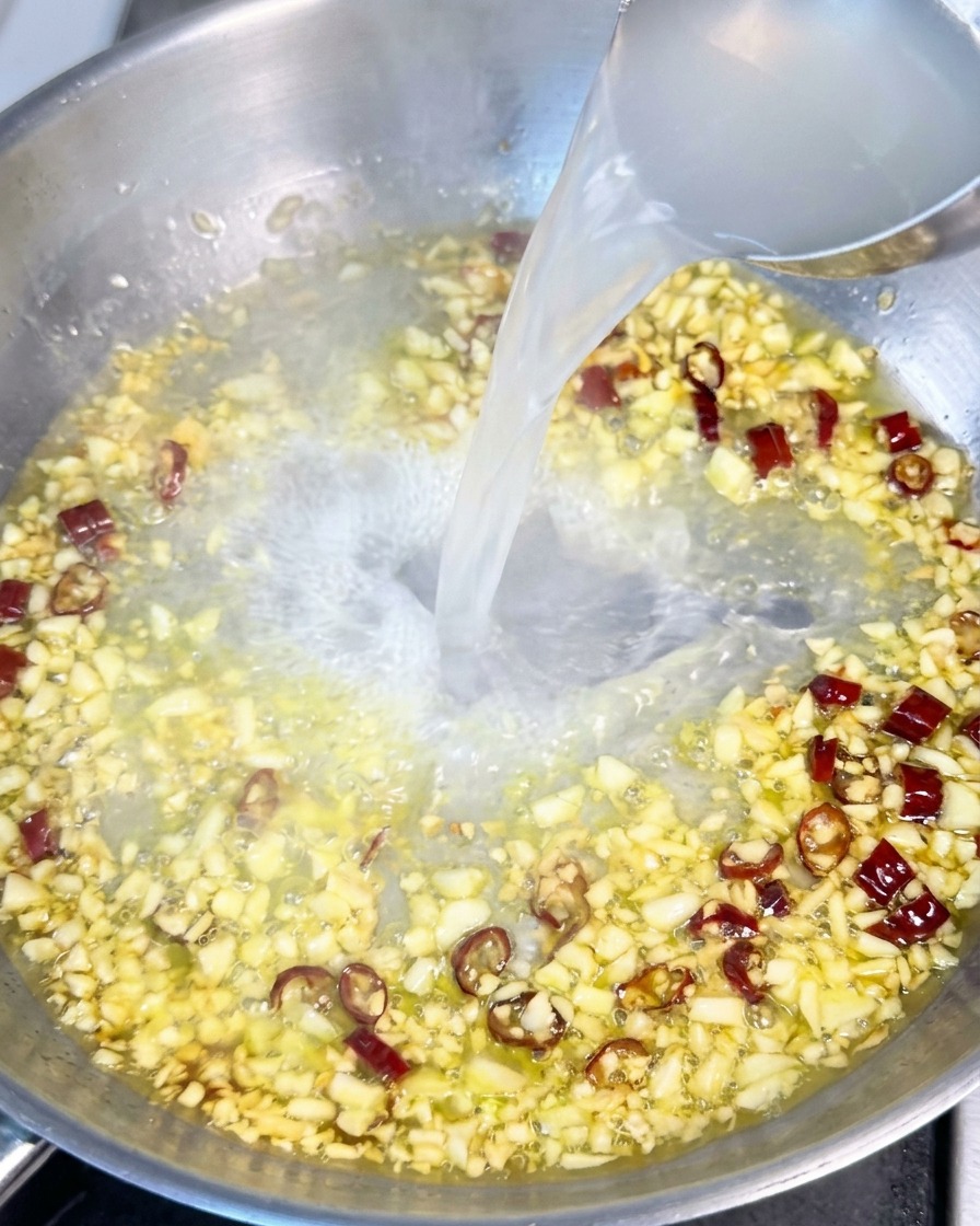 Woda z gotowania makaronu wlewana chochlą na patelnię z czosnkiem, oliwą i suszonym chili.