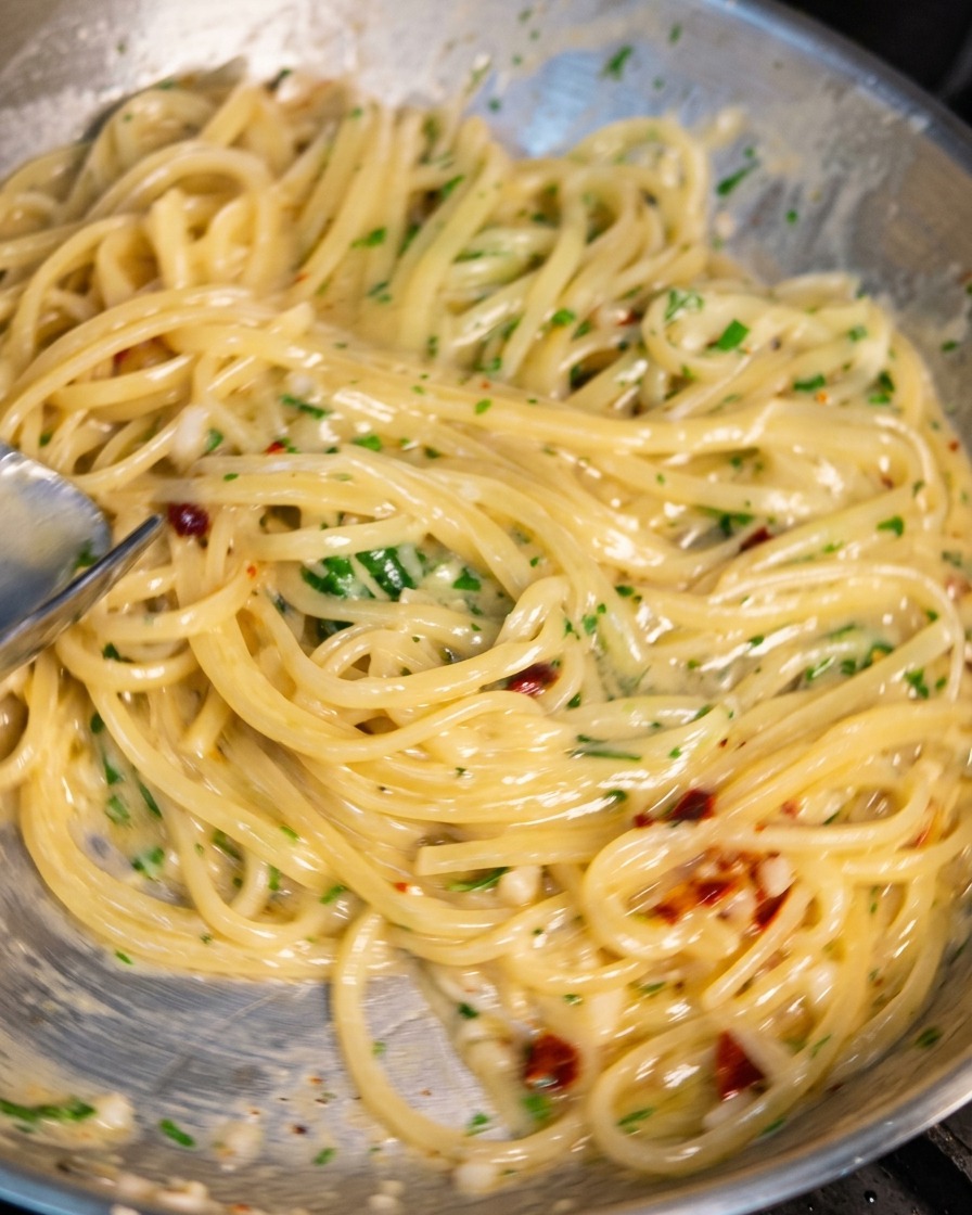 Patelnia ze stali nierdzewnej ze spaghetti mieszanym szczypcami, pokrytym lśniącym, kremowym sosem z czosnkiem, chili i pietruszką.