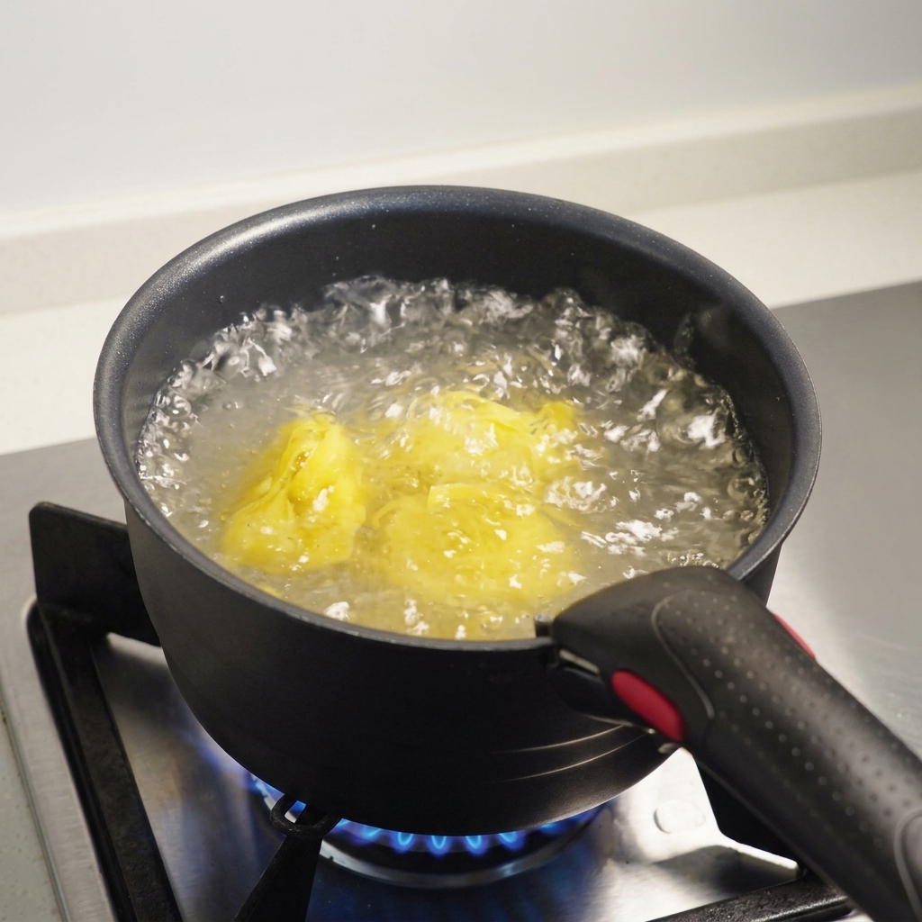 Makaron fettuccine zanurzony we wrzącej, osolonej wodzie w ciemnym garnku na kuchence gazowej.