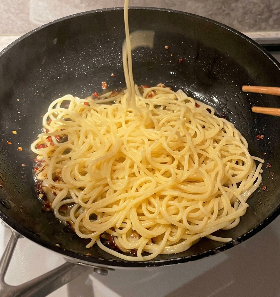 Metalowe sitko przekładające długie nitki ugotowanego makaronu spaghetti bezpośrednio na patelnię z czosnkiem i oliwą.