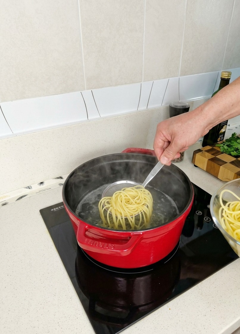 Wyjmowanie gniazda na wpół ugotowanego makaronu spaghetti z czerwonego garnka z parującą wodą przy użyciu małego sitka.