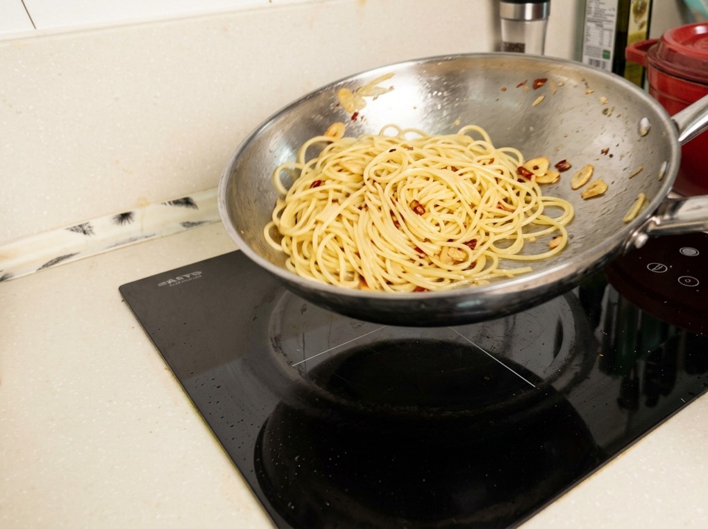 Makaron spaghetti podrzucany na patelni w powietrzu, pokrywający się lśniącym, zemulgowanym sosem.
