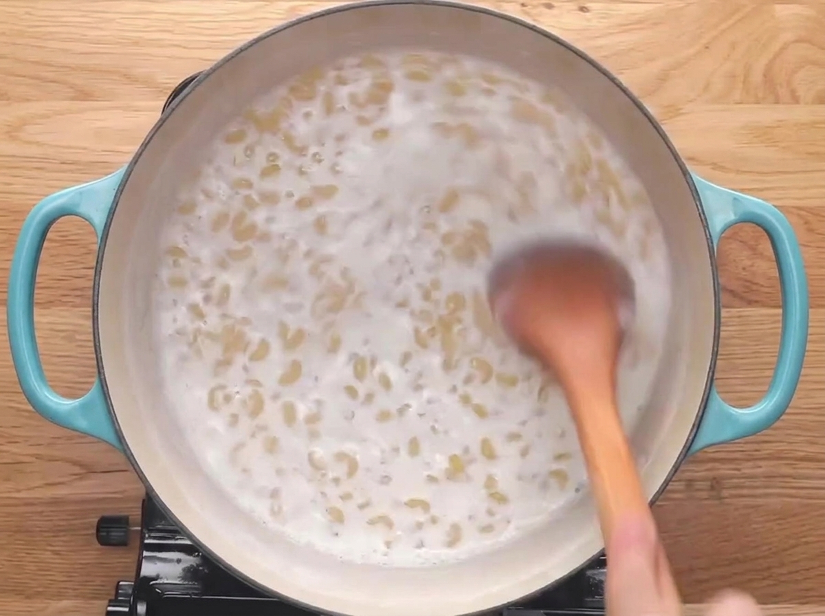 Drewniana łyżka mieszająca makaron kolanka gotujący się w mleku.