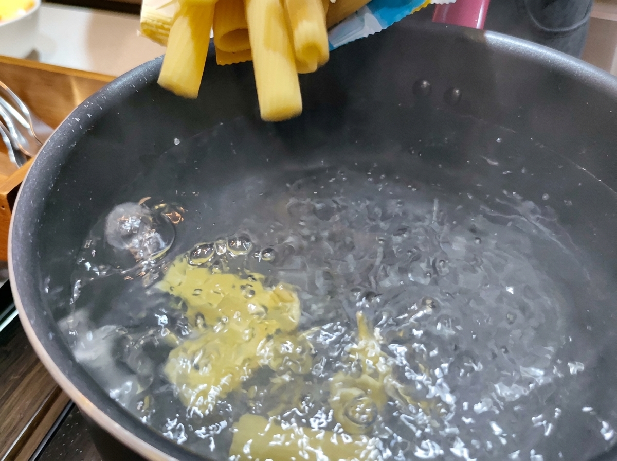 Suchy, żółty makaron Rigatoni wrzucany do garnka z mocno wrzącą wodą.