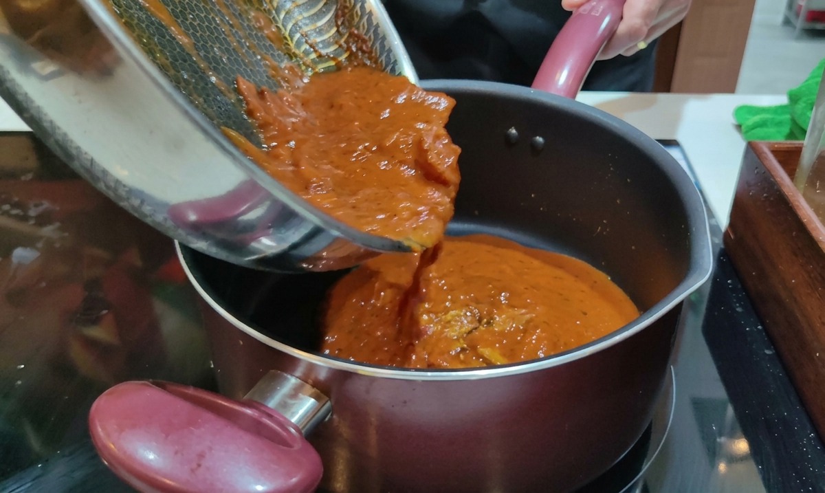 Przelewanie gorącego sosu Amatriciana z patelni do garnka z ugotowanym makaronem Rigatoni.