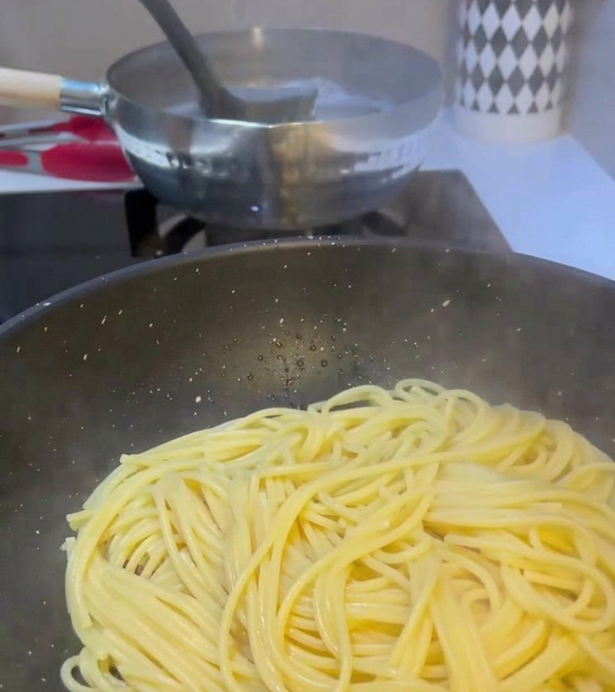 Chochelka przenosi mętną wodę z gotującego się garnka z makaronem na patelnię, na której znajduje się już spaghetti i przygotowane mięso.