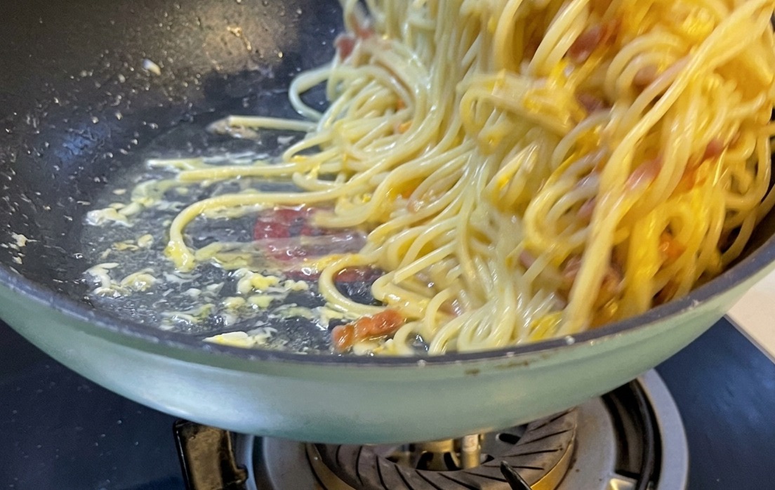 Pięknie podana porcja spaghetti carbonara na białym ceramicznym talerzu, posypana tartym serem i pieprzem.