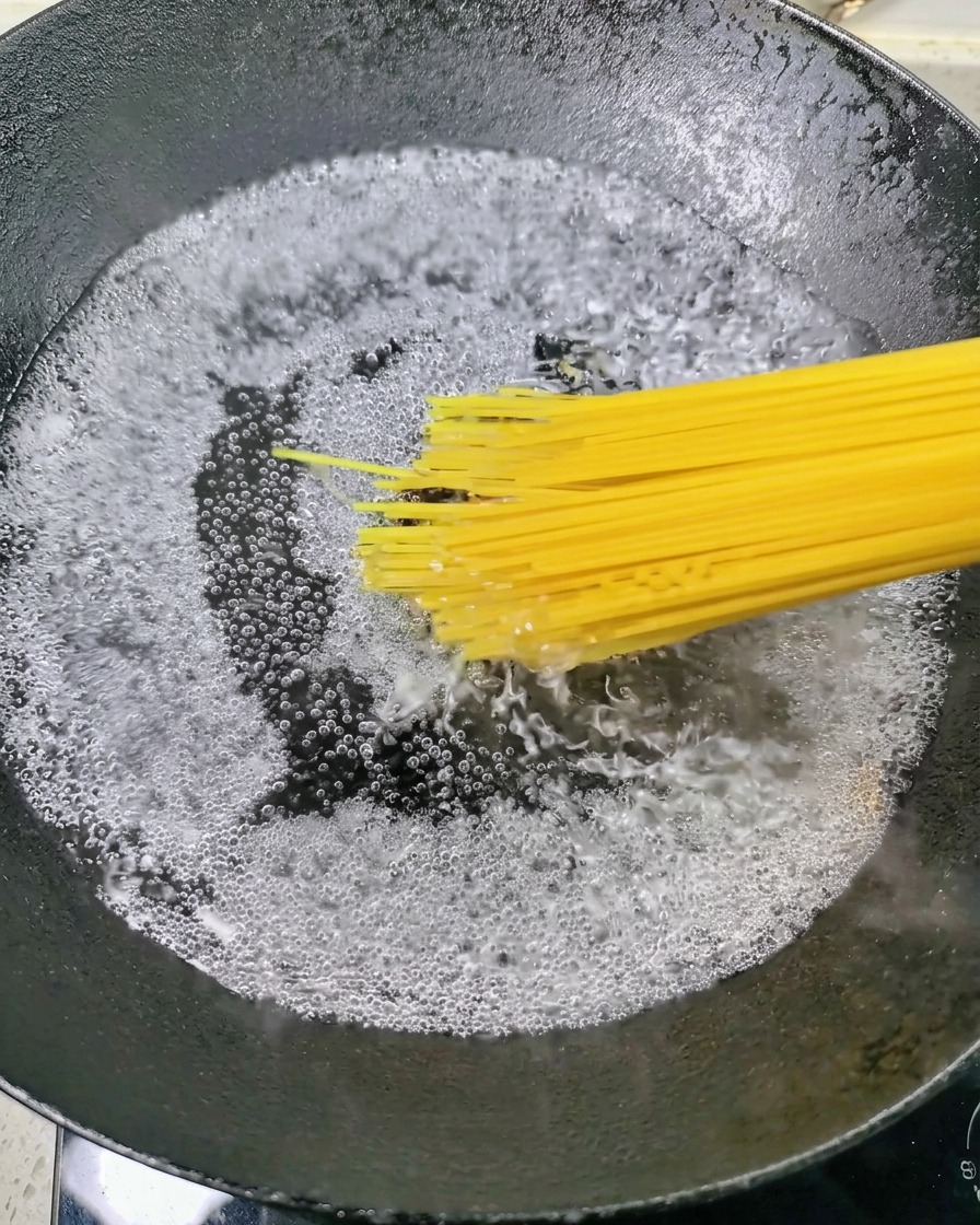 Suchy makaron spaghetti wrzucany do garnka z mocno wrzącą wodą.