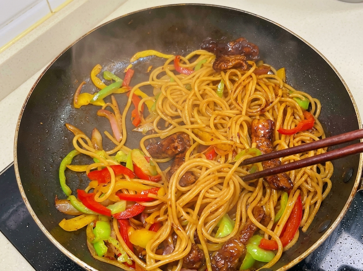 Mieszanie pałeczkami parującego spaghetti, mięsa i papryki w lśniącym, ciemnym sosie.