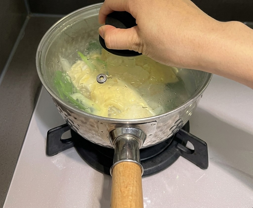 Dłoń nakładająca szklaną pokrywkę na garnek z makaronem i serem, aby zatrzymać parę