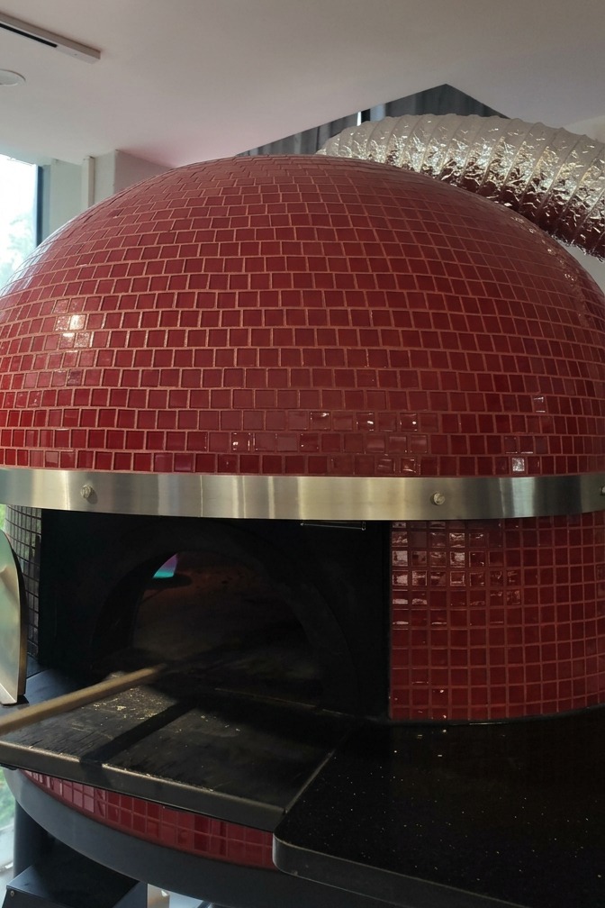 Piec opalany drewnem z wykończeniem z czerwonych kafelków, do którego wsuwana jest pizza na długiej metalowej łopacie.