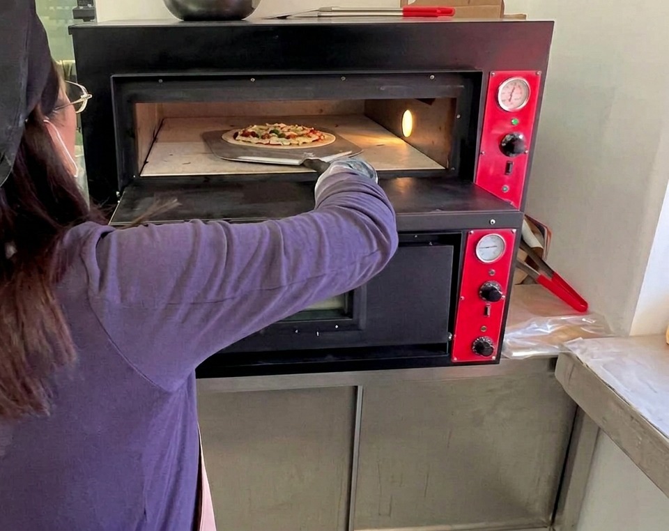 Kucharz wsuwający surową pizzę Margherita do gorącego, profesjonalnego pieca za pomocą długiej metalowej łopaty.