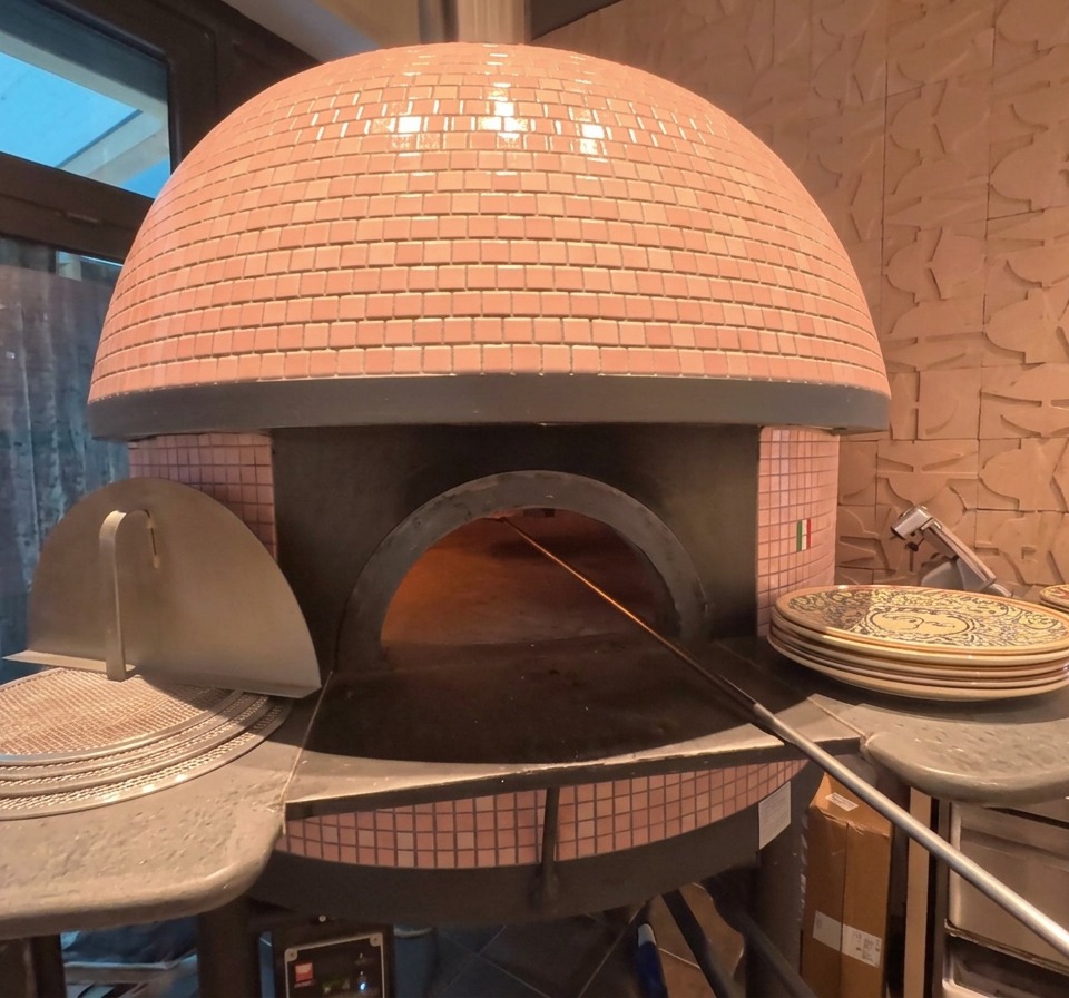 Kopuła różowego pieca do pizzy z widocznym w środku piekącym się plackiem tuż obok żarzących się polan.