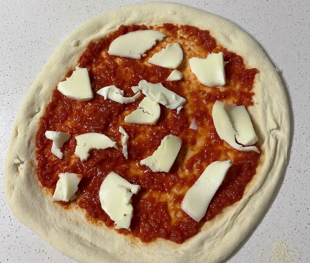 Rwanie dłońmi białej świeżej mozzarelli na kawałki i układanie ich na spodzie do pizzy pokrytym czerwonym sosem pomidorowym.
