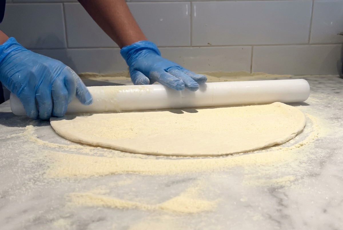 Biały wałek rozciągający cienki spód pizzy na marmurowym stole posypanym mąką.