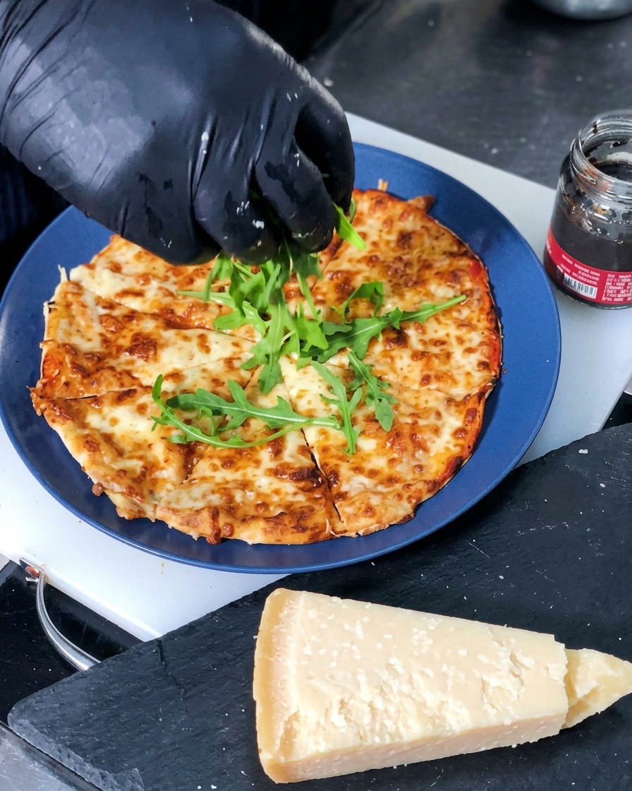 Świeże, zielone liście rukoli układane na środku pokrojonej, świeżo upieczonej pizzy z serem.