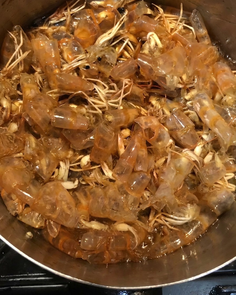 Skorupki krewetek gotujące się w ciemnej mieszance sosu w garnku.