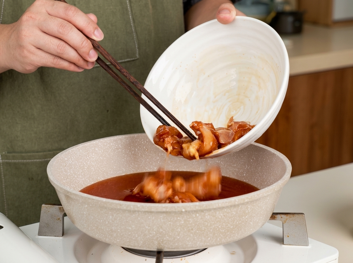 Kawałki kurczaka dodawane do patelni z mieszanką sosu teriyaki za pomocą pałeczek.