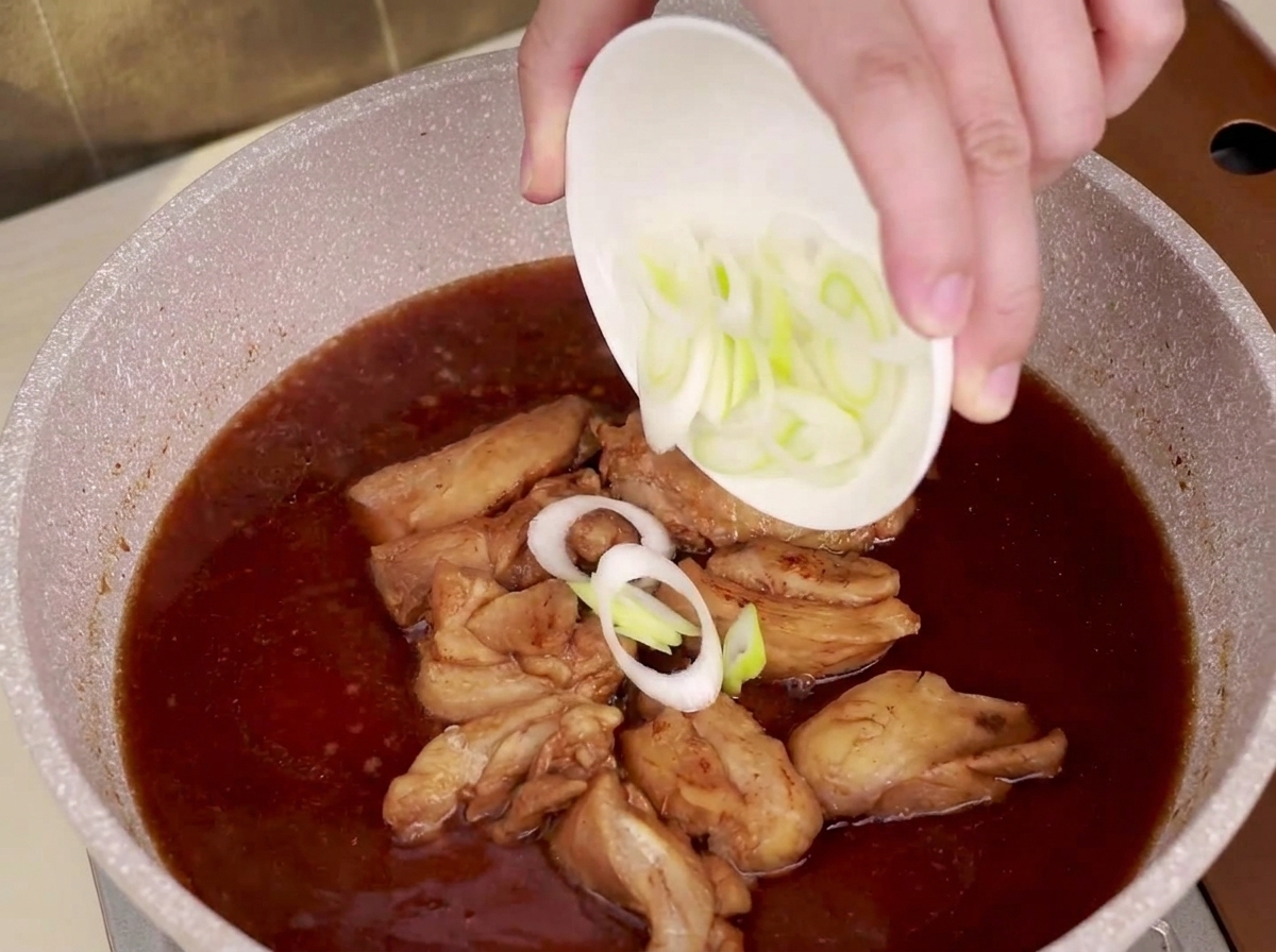 Pokrojony por posypywany do patelni z duszącym się kurczakiem w sosie teriyaki.