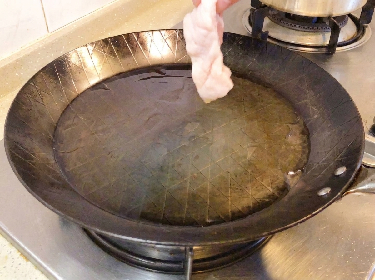 Surowe podudzie z kurczaka skórą do dołu na gorącej patelni.