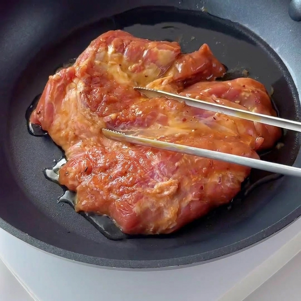 Zamarynowany kotlet schabowy skwierczący i rumieniący się na ciemnej patelni z powłoką nieprzywierającą.