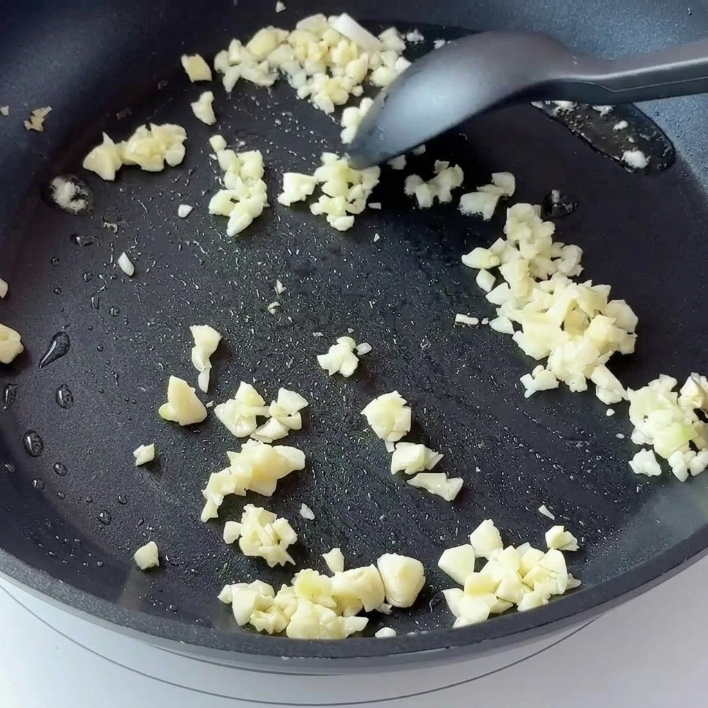Posiekany czosnek i pokrojona w kostkę cebula smażone na ciemnej patelni.