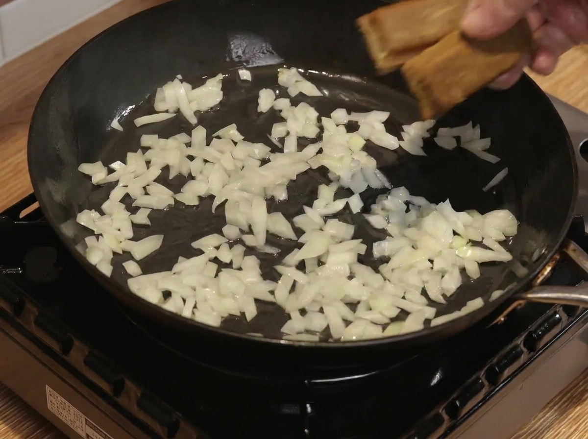 Kostki curry i woda mieszane z podsmażoną cebulą na patelni.
