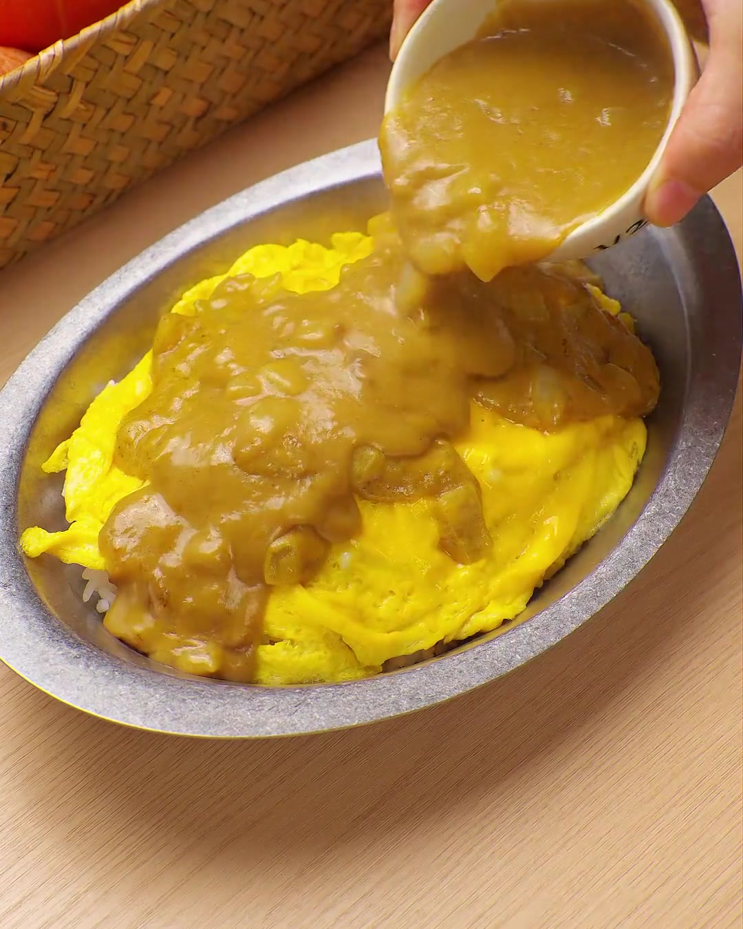 Bogaty, żółty sos curry wylewany z małej miseczki na porcję ryżu z jajecznicą.