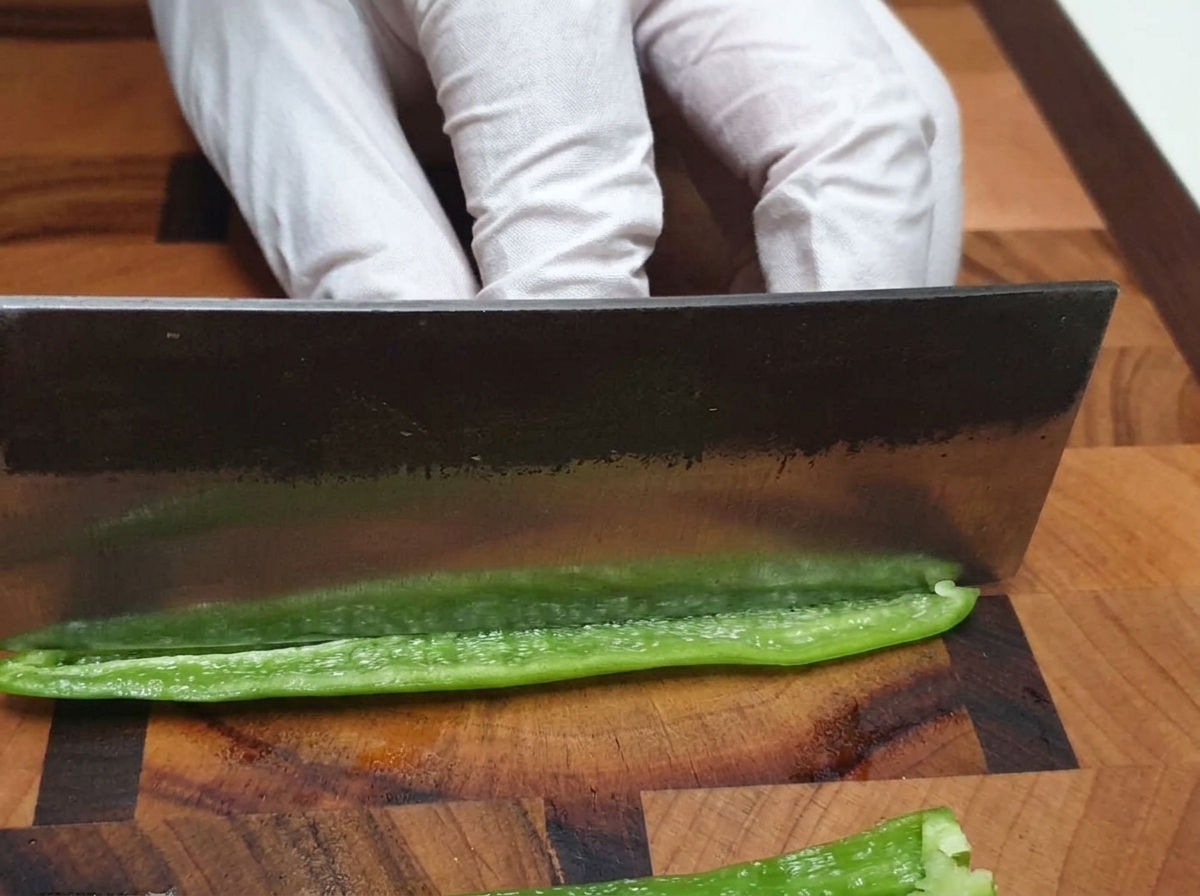 Nóż szefa kuchni drobno siekający zieloną papryczkę chili na drewnianej desce.