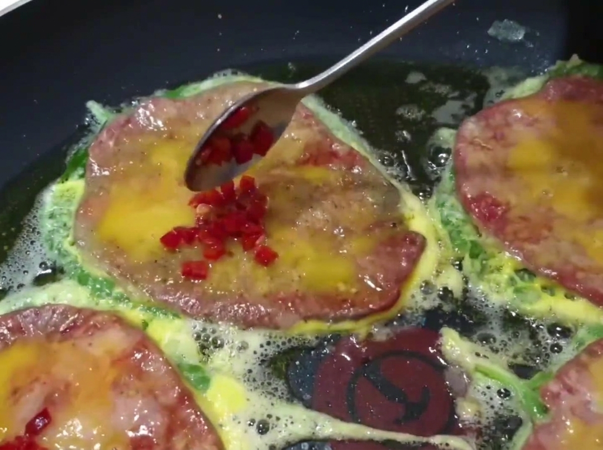 Zbliżenie na łyżkę dodającą drobno pokrojone papryczki chili na wierzch smażących się placków.