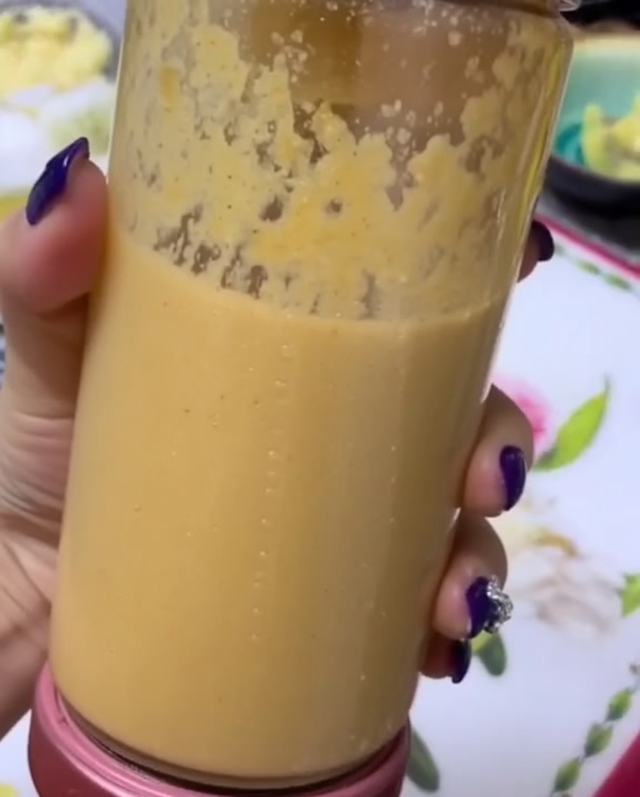 Dłoń trzymająca przezroczysty kielich blendera wypełniony gładkim, gęstym puree z owoców i warzyw.