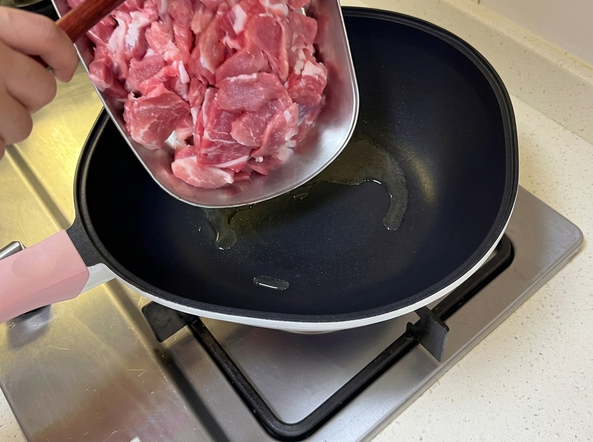 Cienko pokrojona wieprzowina dodawana na gorącą patelnię z rozgrzanym olejem.