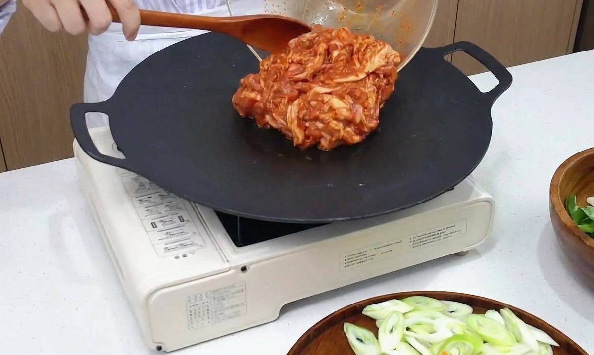 Marynowany pikantny boczek wylewany ze szklanej miski na gorącą patelnię typu grill.