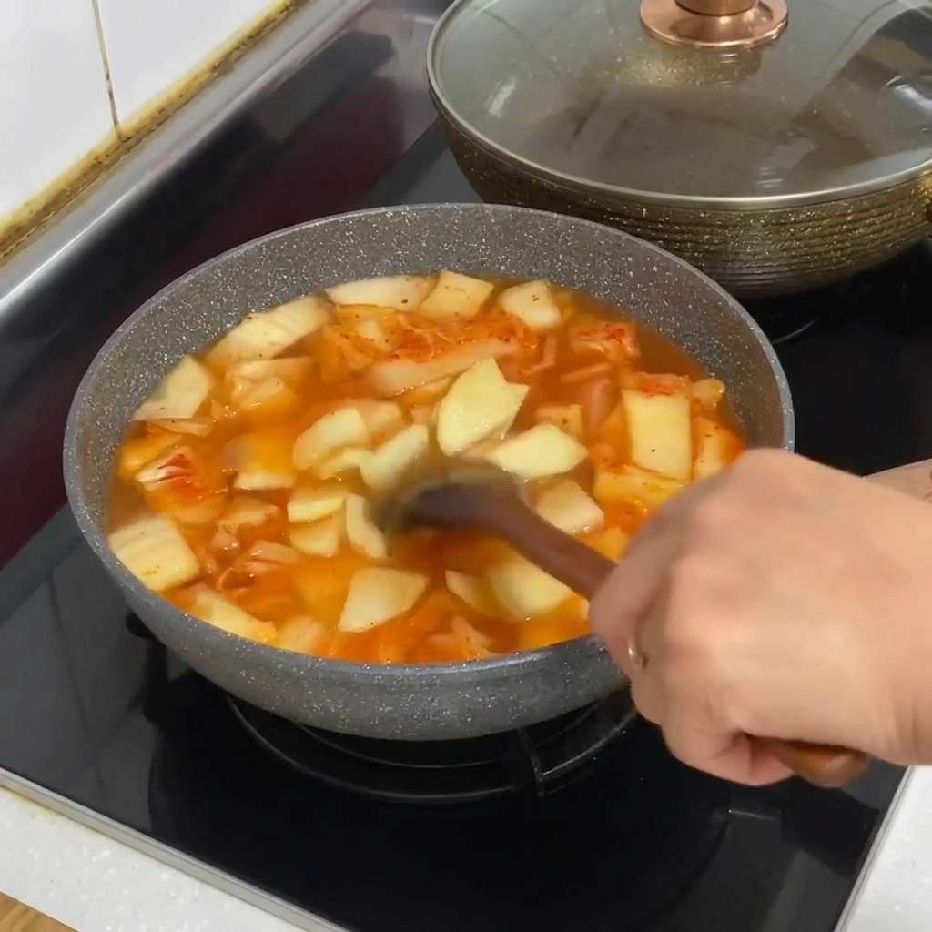 Makaron sojowy dodawany do garnka z gotującą się zupą kimchi.