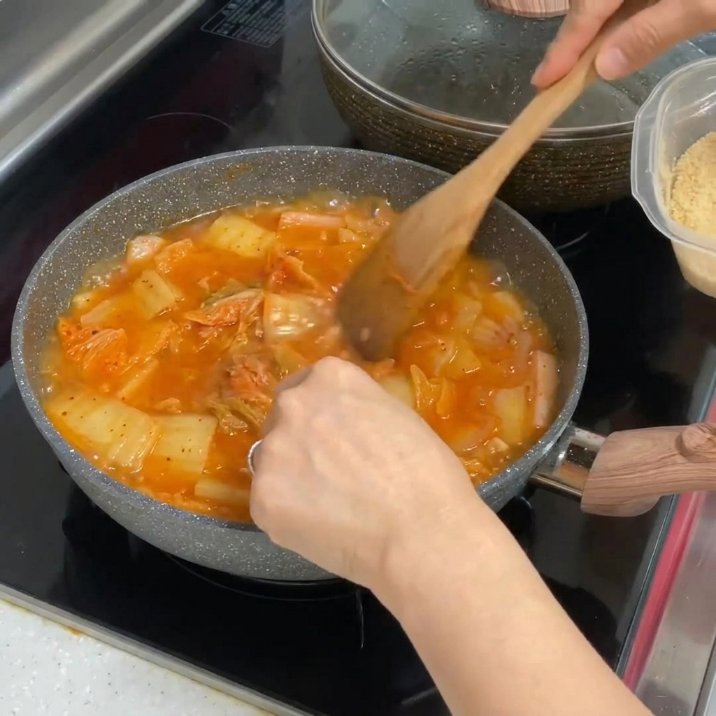 Posiekany czosnek dodawany do garnka z żywo czerwoną, bulgoczącą zupą kimchi.