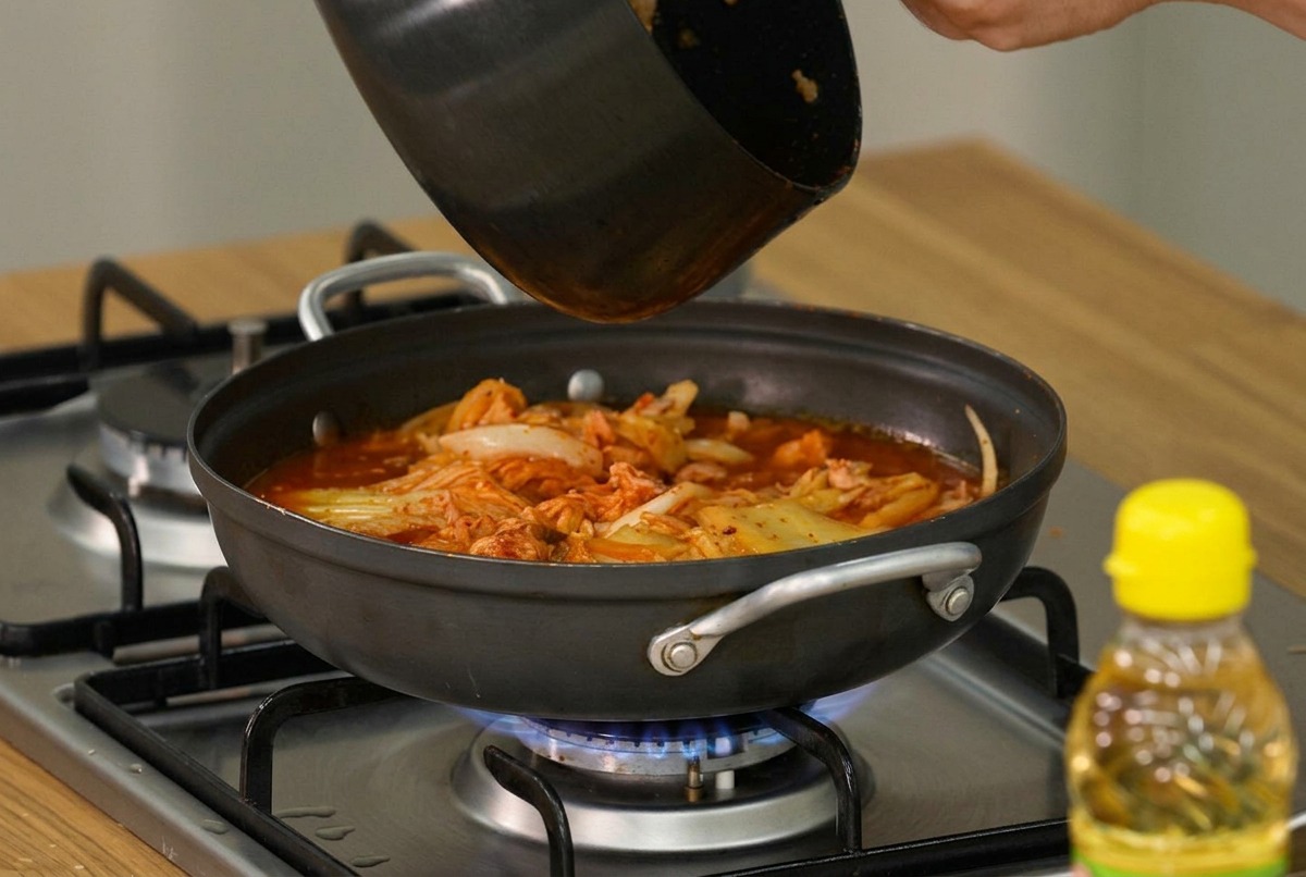 Plastry miękkiego tofu i świeża posiekana dymka układane na wierzchu gotującego się gulaszu kimchi.