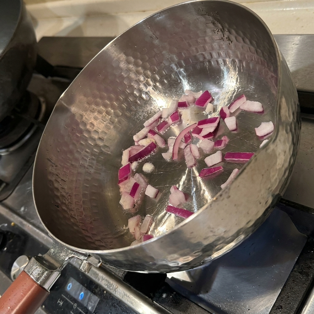 Kawałki cebuli podsmażane na patelni z olejem, stające się miękkie i aromatyczne.