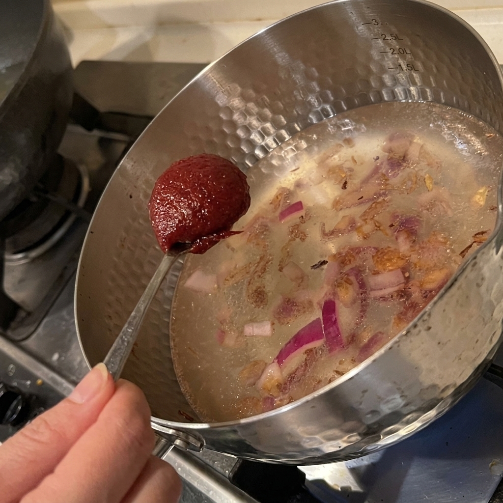 Łyżka koreańskiej pasty chili dodawana do garnka z wodą i podsmażoną cebulą.
