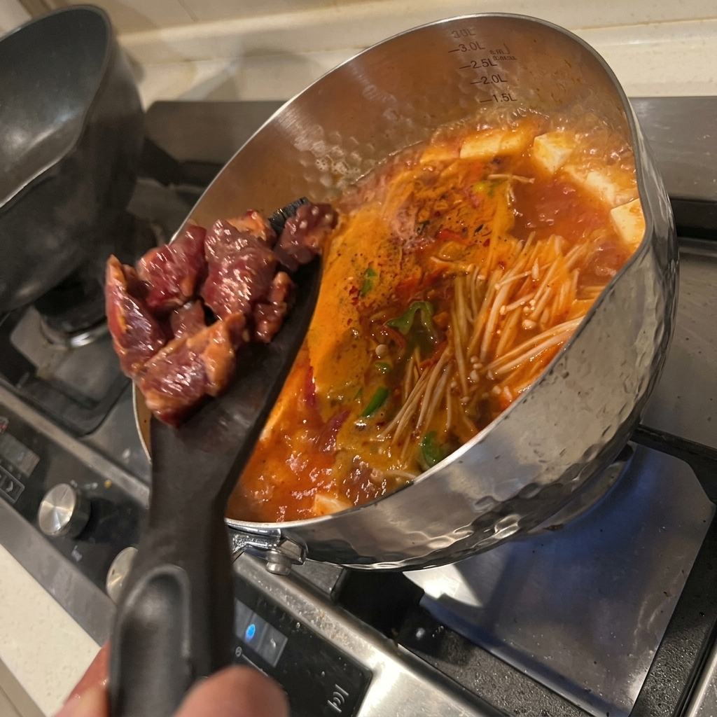Zamarynowane kawałki wołowiny wrzucane do wrzącej zupy kimchi z tofu.