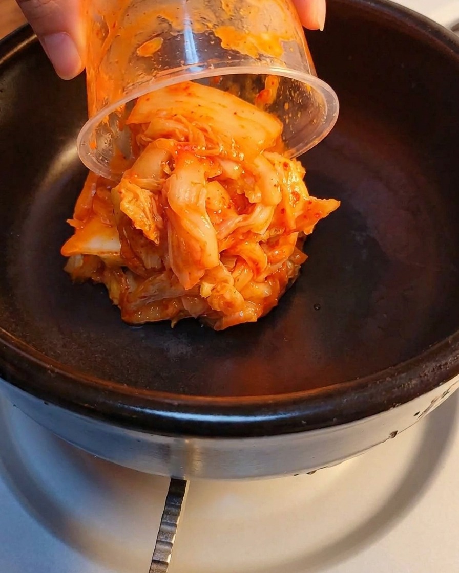 Fermentowane kimchi i rozgnieciona mielonka warstwowo w kamiennym garnku.