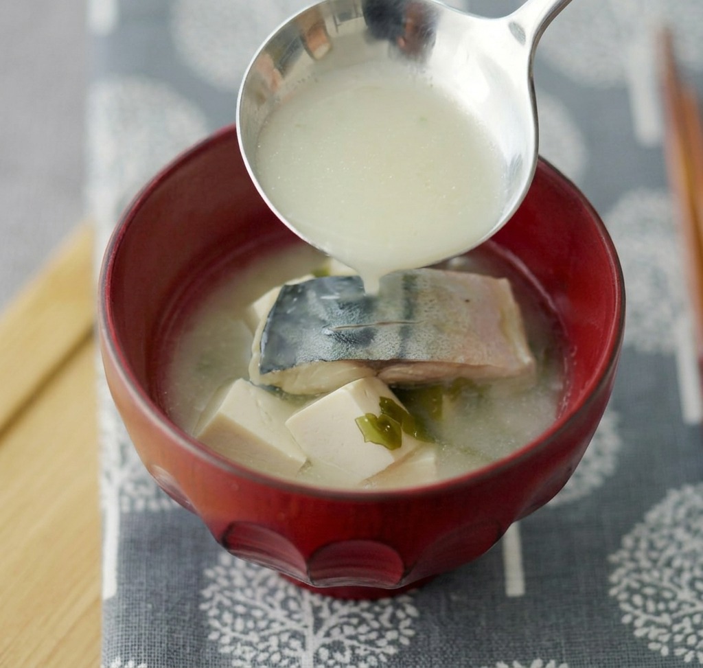 Zupa miso z makrelą i tofu serwowana w głębokiej czerwonej miseczce ceramicznej.