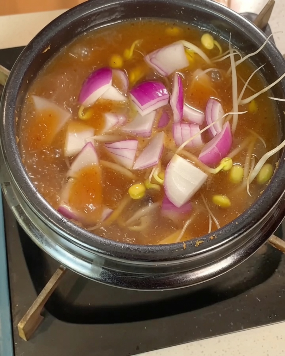 Kiełki fasoli, cebula i kostki tofu gotujące się w bulionie.