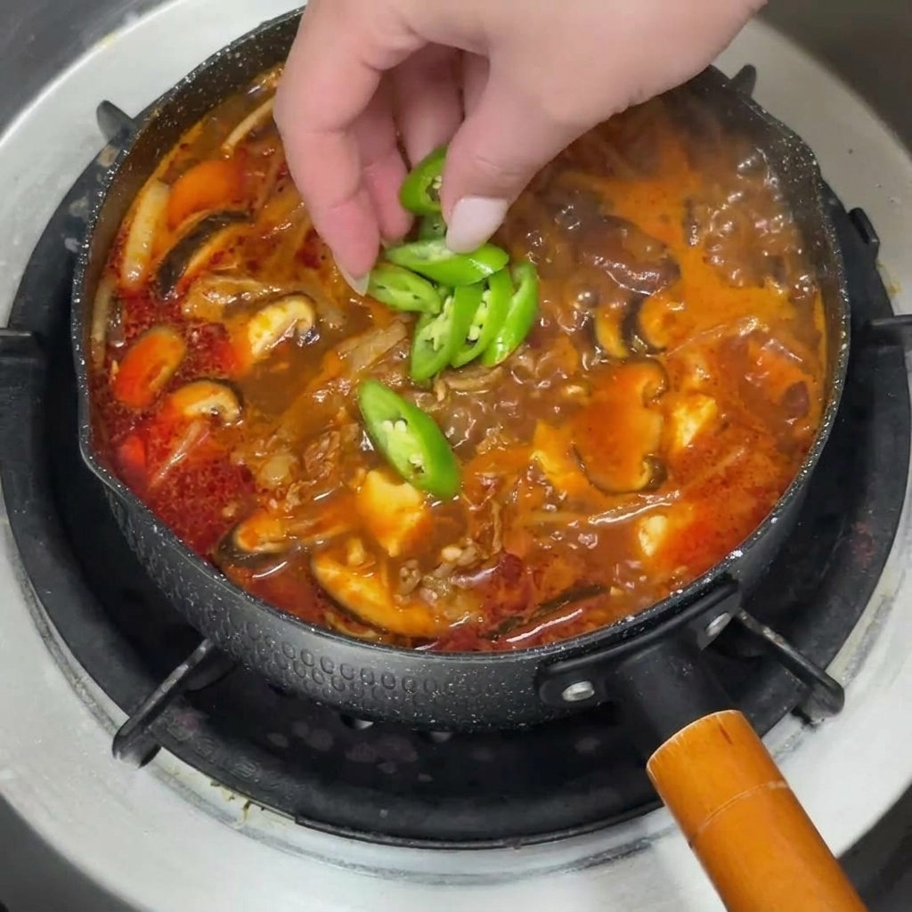 Gorący garnek gulaszu wołowego udekorowany świeżymi plasterkami zielonego chili i posiekaną dymką.