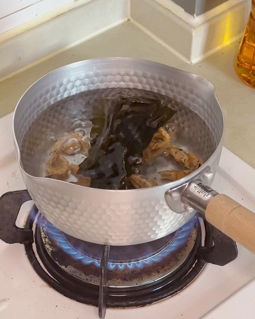 Zbliżenie na suszone krewetki i ciemny kawałek wodorostu kelp zanurzone w wodzie w garnku.