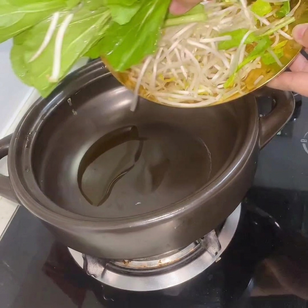 Świeży bok choy i kiełki fasoli smażone w rozgrzanym glinianym garnku.