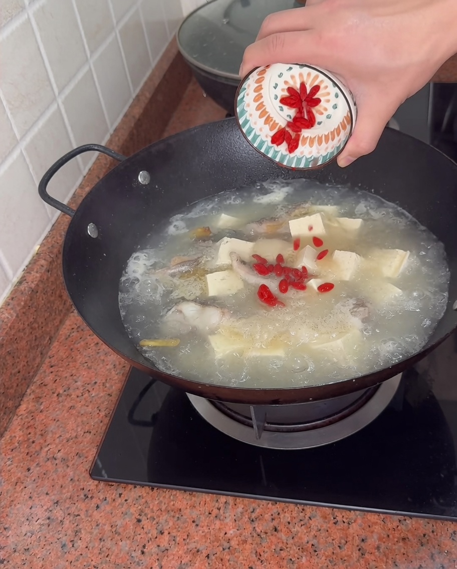 Wsypywanie czerwonych jagód goji z małej miseczki do bulionu z rybą i tofu.
