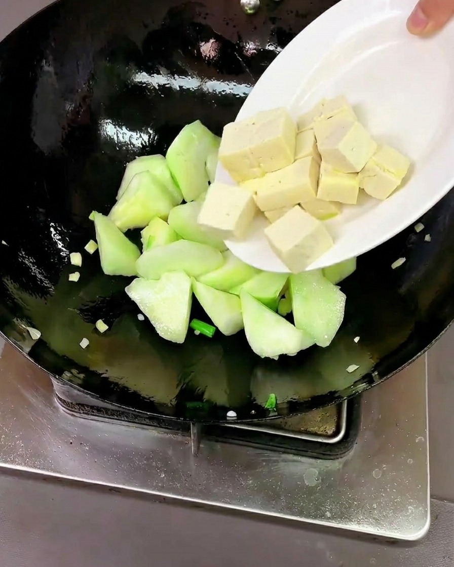 Świeże kostki tofu i surowe małże dodawane do woka z luffą.