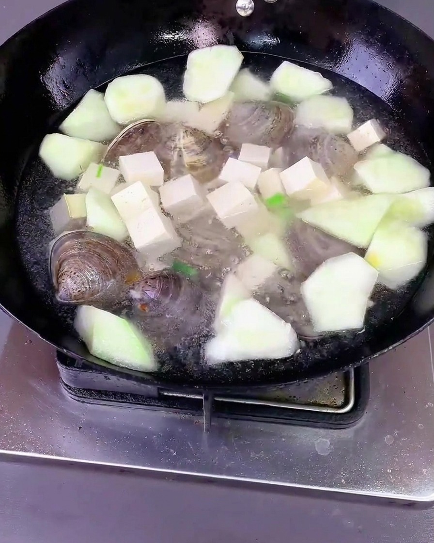 Woda wlana do woka z luffą, tofu i małżami, przykryta pokrywką.